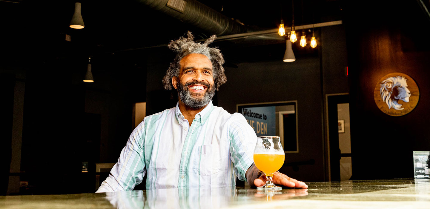smiling man drinking golden beer at bar