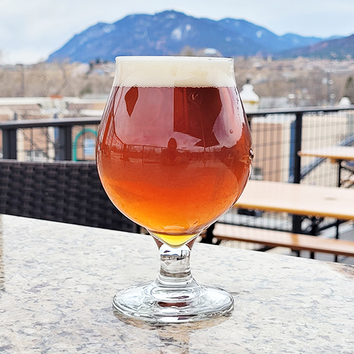 ale in snifter glass on patio with mountains in the background
