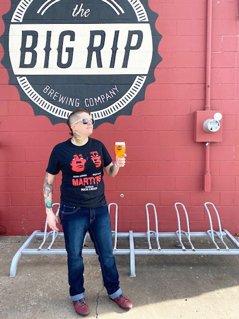 woman with beer posing in front of the big rip brewing