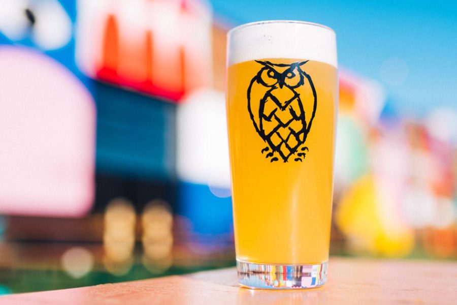 hazy beer in glass with owl logo against abstract colorful blurry background